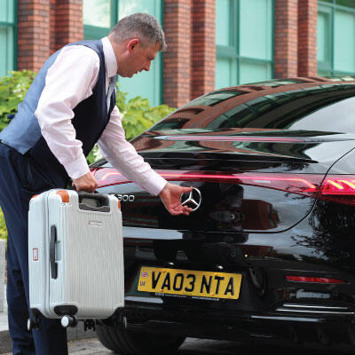 Professional chauffeur assisting with luggage at an airport transfer.